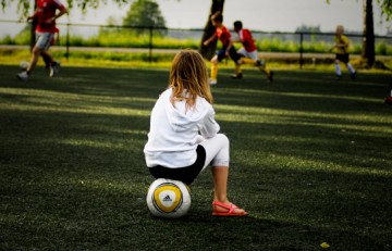 Nena mirant un partit de futbol asseguda sobre una pilota - Tjook - Flickr  CC BY ND-2.0