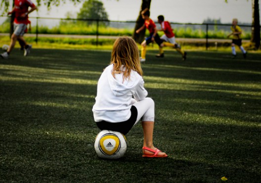 Nena mirant un partit de futbol asseguda sobre una pilota - Flickr - CC BY-ND 2.0