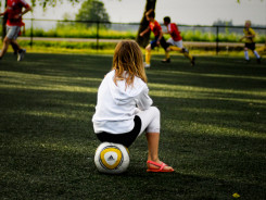 Nena mirant un partit de futbol asseguda sobre una pilota - Flickr - CC BY-ND 2.0